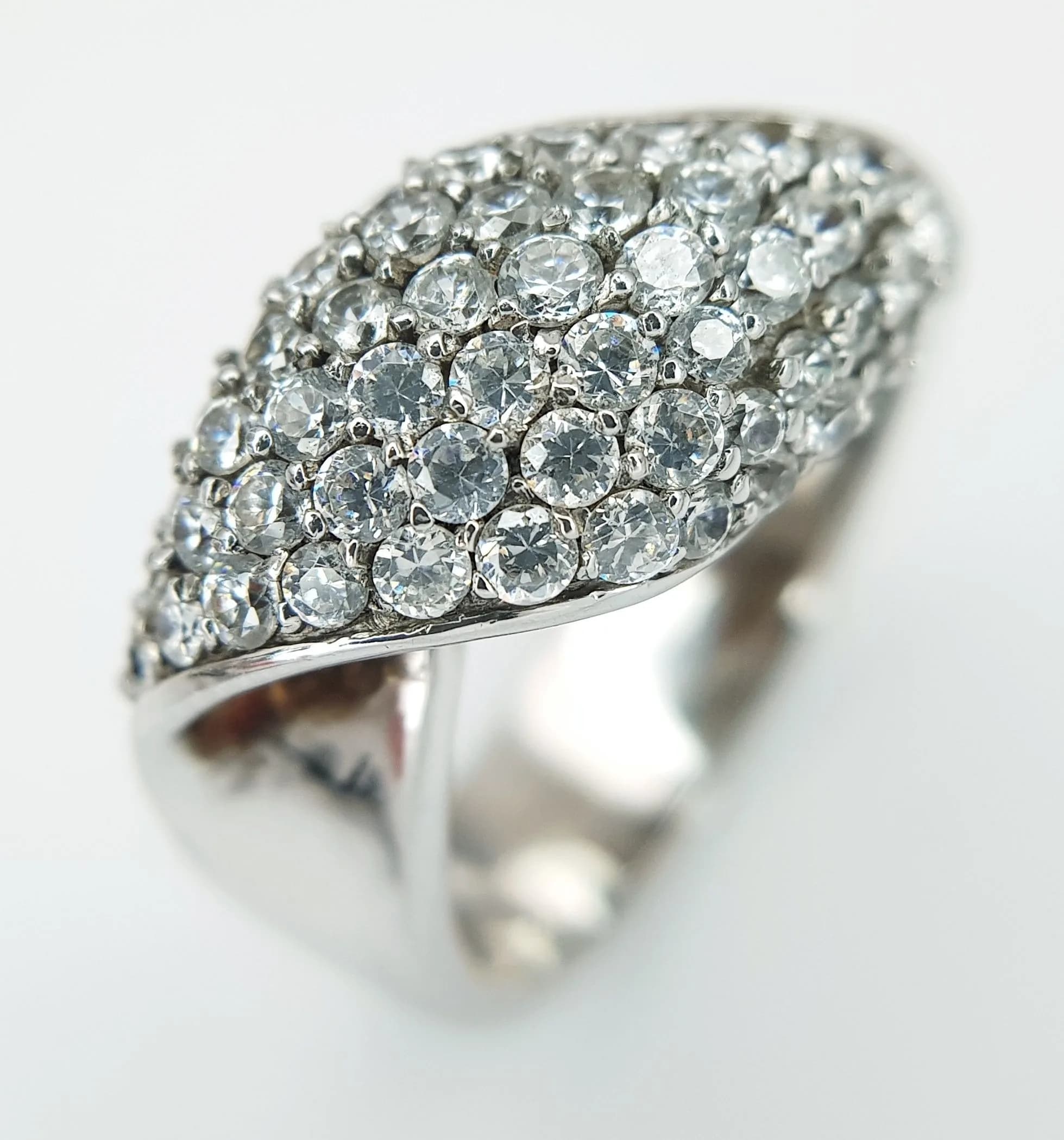 A 925 Silver White Stone Dress Ring. Polished crossover band set with a large white stone pavé panel. Hallmarked 925. Ring size Q. Total weight 9.15 grams.