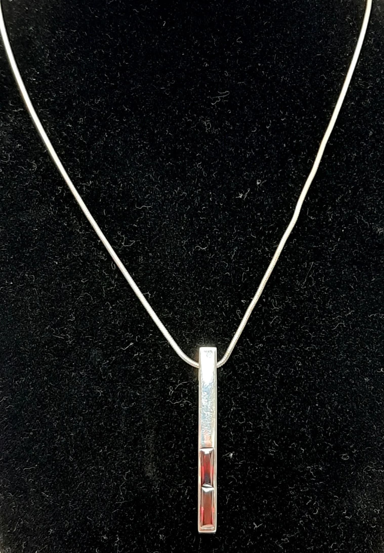 A 925 Silver Red Stone Bar Pendant Necklace. Rectangular bar pendant set with two red stones, on a 47cm snake chain. Pendant measures 4.5cm drop. Hallmarked 925. Total weight 8.73 grams.