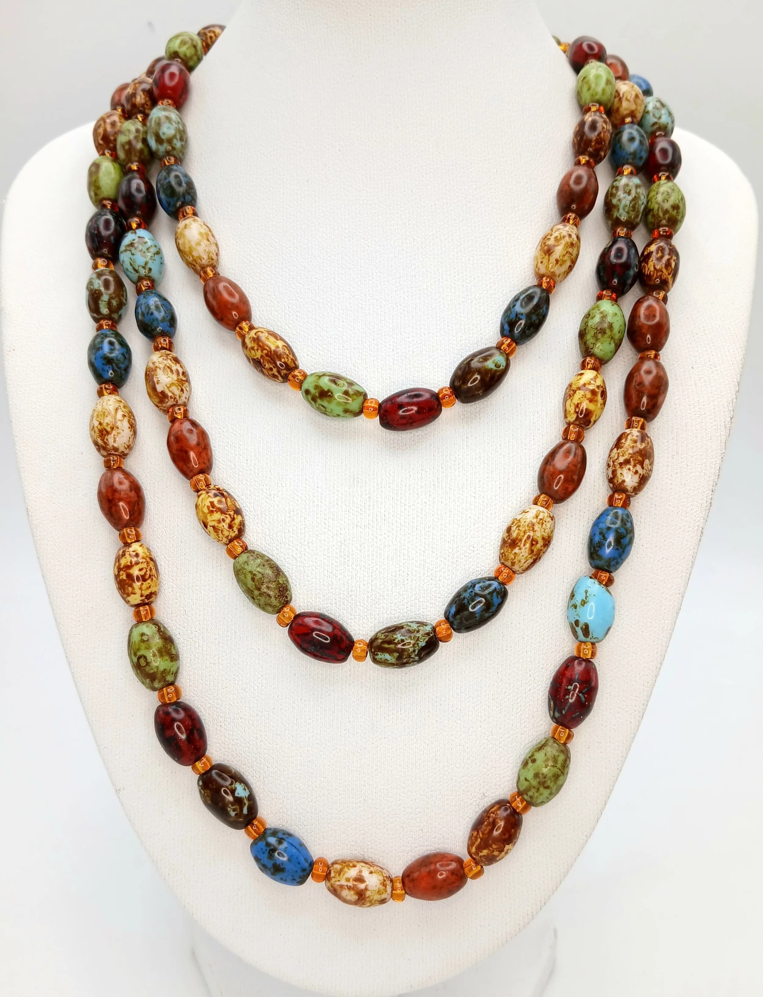 A Colourful Long Multi-Coloured Beaded Necklace. Set with oval beads in assorted blue, green, amber, red and brown tones, interspersed with small spacer beads. The necklace measures approx. 120cm length.