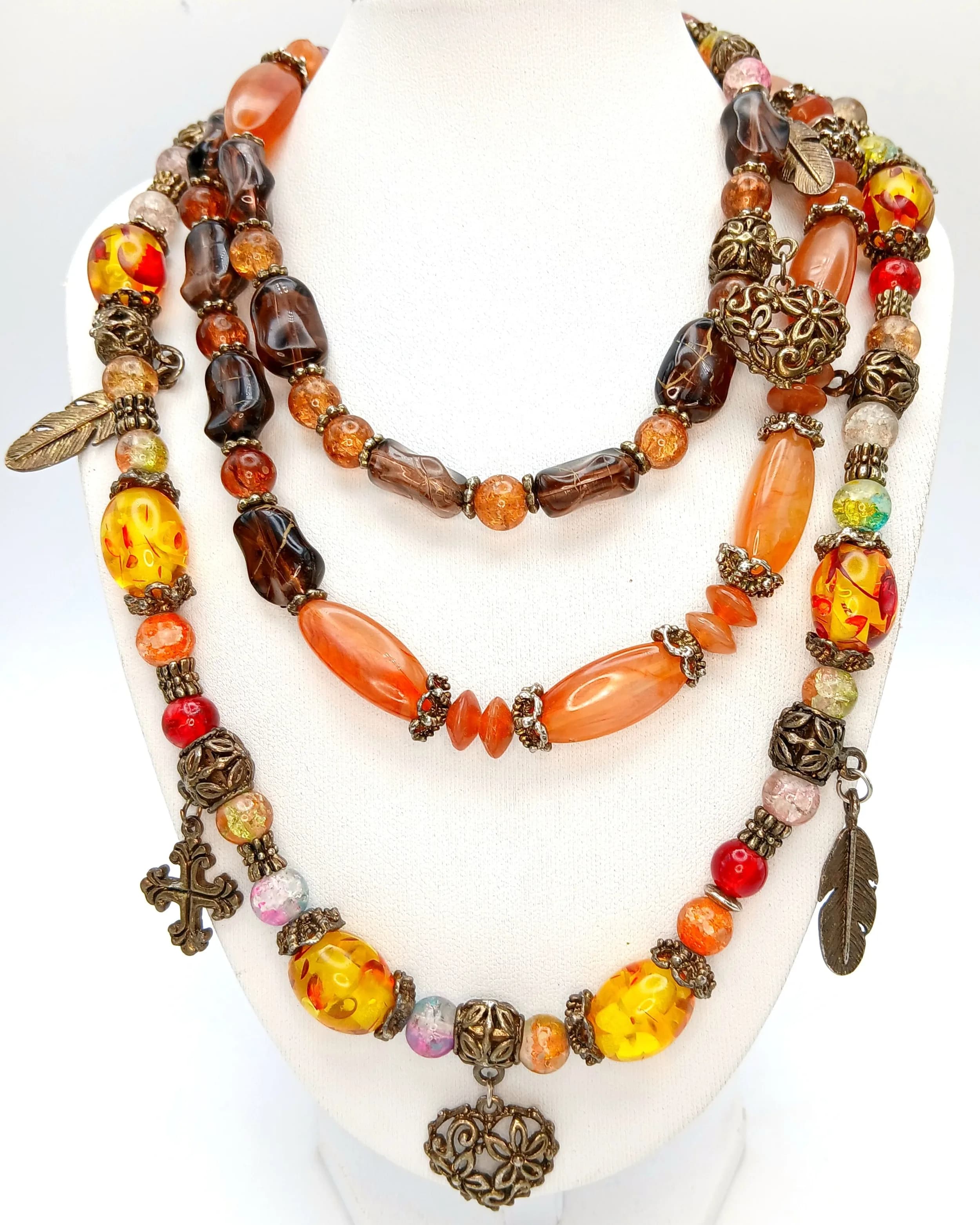 A Pretty Long Multicoloured Beaded Necklace. Set with assorted amber, brown, orange and multicoloured glass beads with silver-tone decorative spacers and assorted leaf, floral and cross charms. Approx. 112cm length.