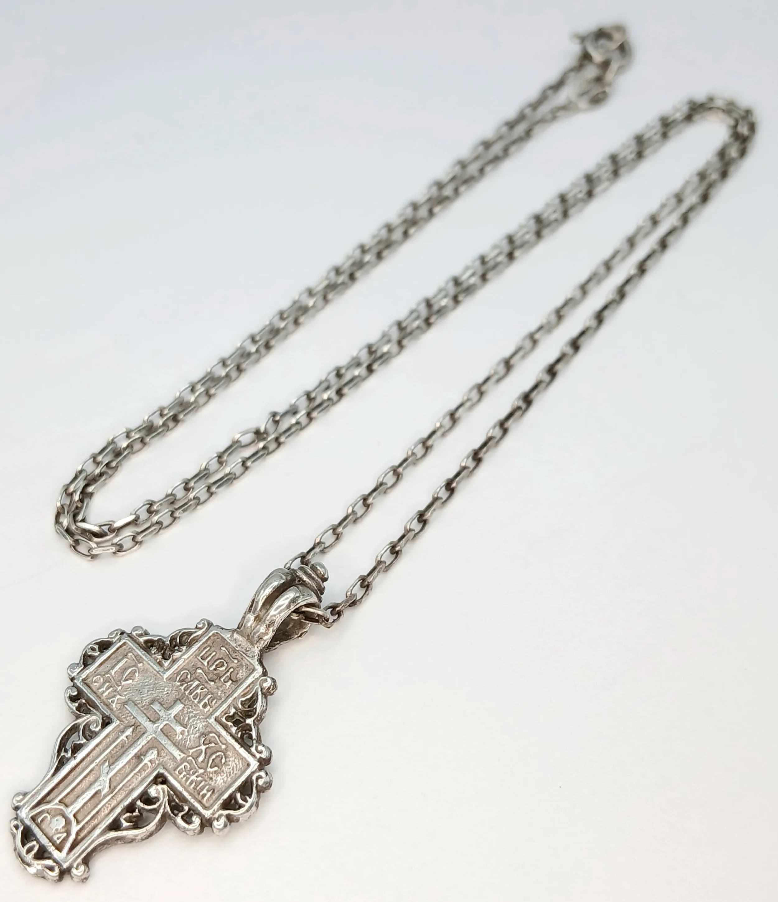 A Decorative 925 Sterling Silver Orthodox Cross Pendant Necklace – 50cm Length. The ornate cross pendant is decorated with religious inscriptions and detailed scrollwork. The pendant measures 3cm x 2cm. Gross weight 5.44 grams.