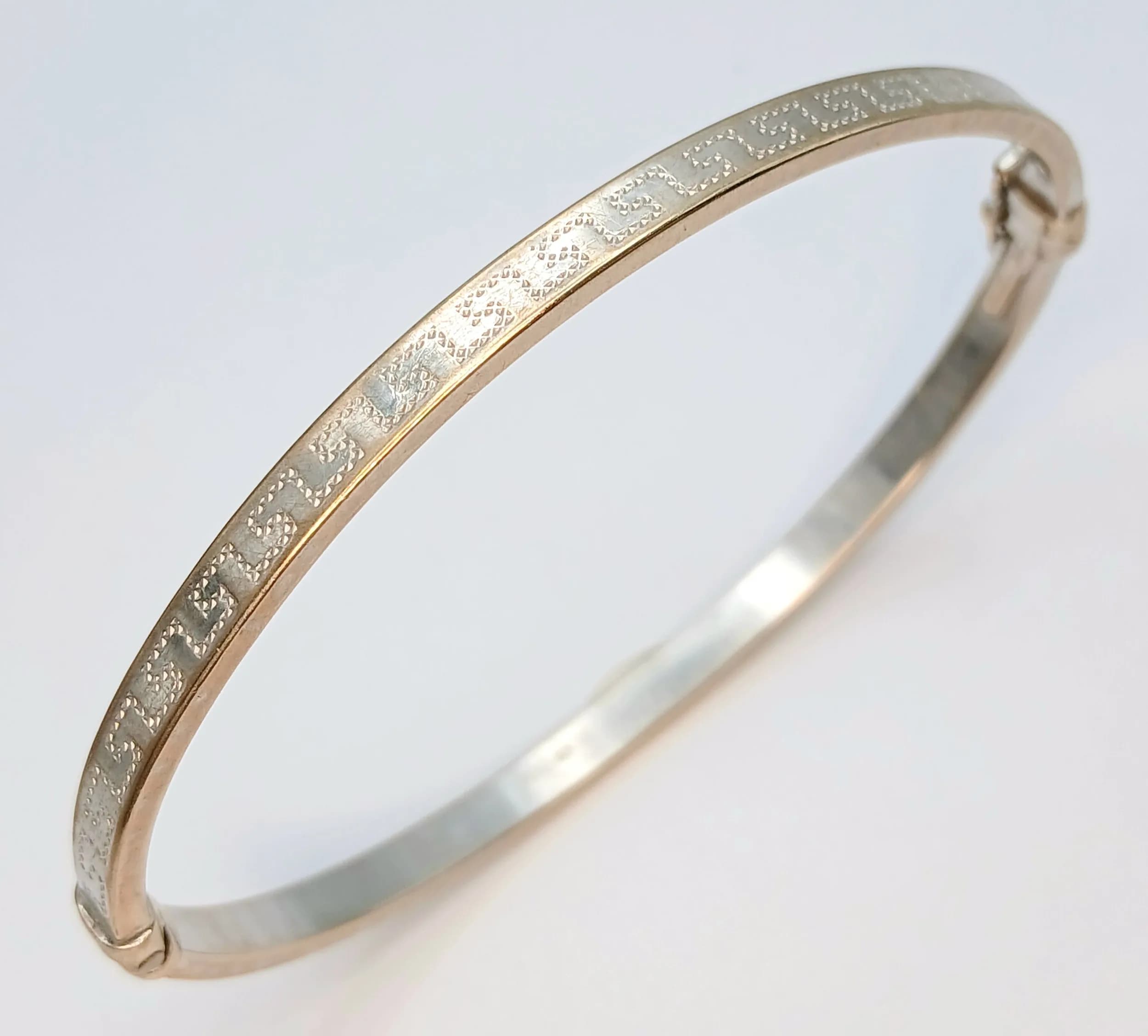 A WHITE AND YELLOW 9K GOLD OVAL SHAPED HINGED BANGLE WITH GEOMETRIC PATTERN TO BOTH SIDES . 5.7gms