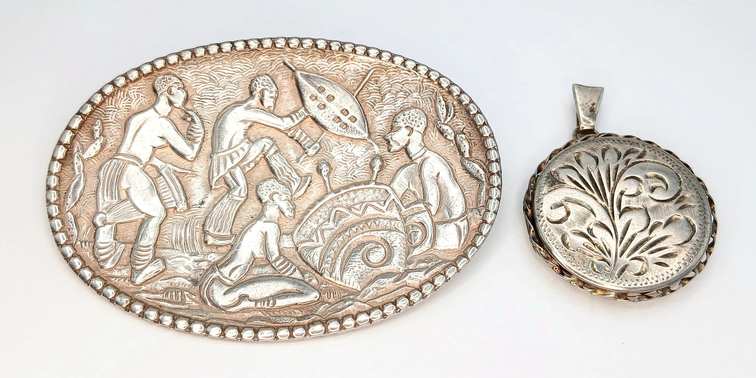 A Sterling Silver Oval Brooch with Tribal Repoussé Decoration PLUS a Sterling Silver small locket pendant. Brooch -5cm. Pendant - 3cm. 14.7g total weight.