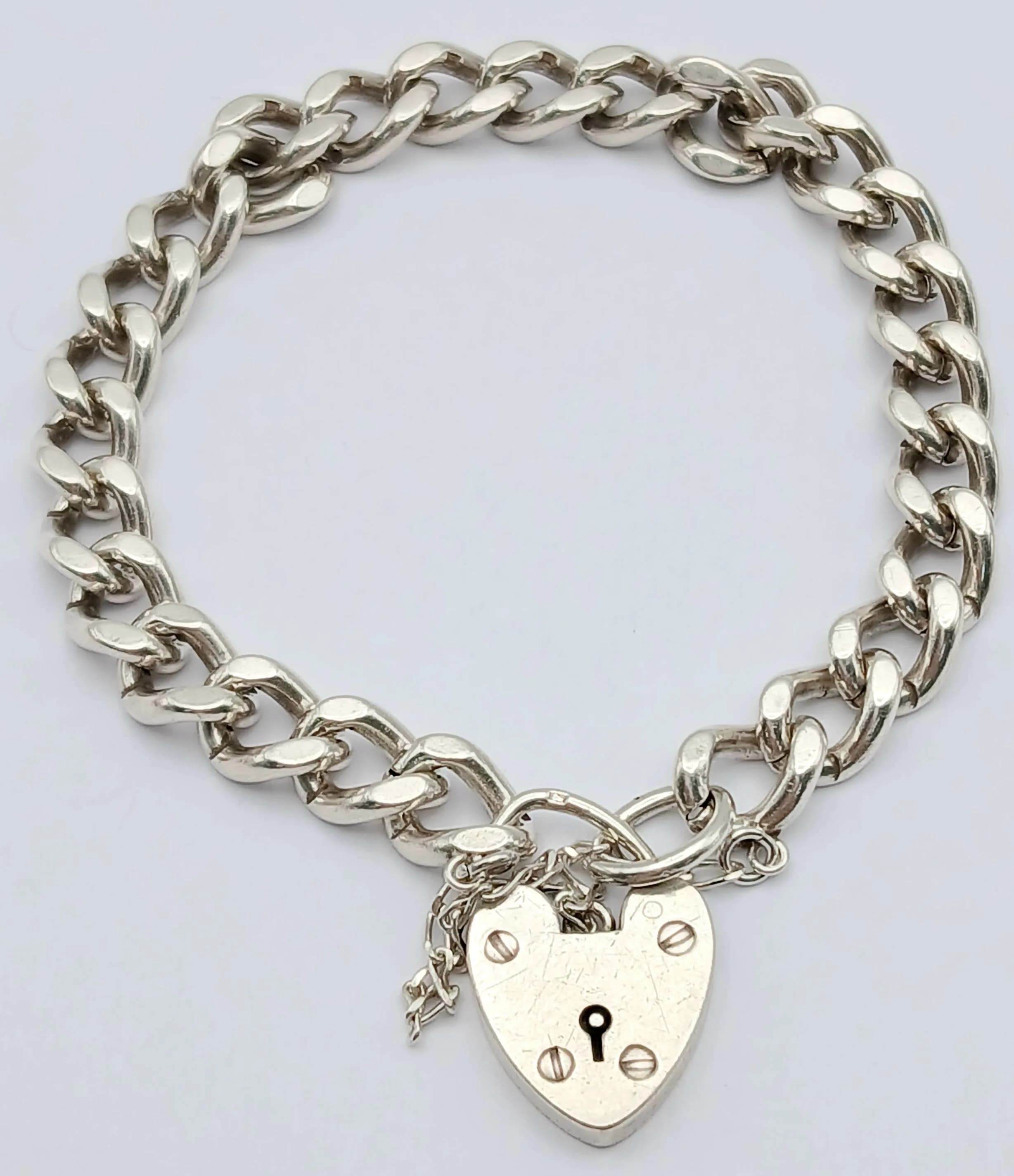 A CHUNKY CURB LINK SILVER BRACELET WITH DISTINCTIVE HEART PADLOCK . 29.1gms 18cms
