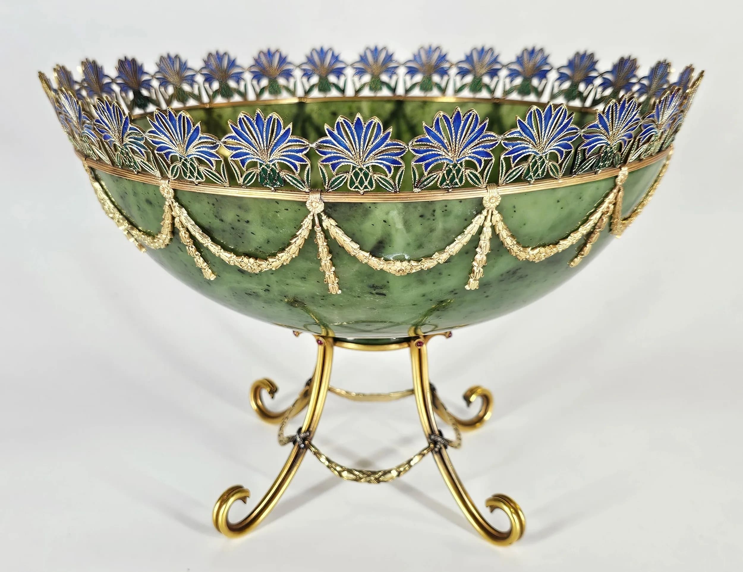 A Magnificent 15K Solid Gold, Nephrite Jade, Diamond and Plique-à-Jour Enamel Russian Style Bowl by Simon Rudle. The large 20th century bowl features a finely carved nephrite jade body applied with laurel garlands suspended from a reeded 15K solid gold ring and raised on a solid gold stand. The top is set with thistle-shaped plique-à-jour enamel, with platinum junctions set with diamonds to the stand. Laser tested as 15K gold, with approximately 300+ grams of gold. Signed Rudle. Nephrite jade in excellent condition. Size approx: 18cm height x 25.5cm width. Impressive total weight: 1060g. Winning bidder must collect from Cadmore HQ or arrange a courier. *Simon Rudle was a Russian-born jeweller from Odessa, Ukraine, later working in New York from the 1970s to 2000s. He came from a distinguished jewellery family and was known for Fabergé-style craftsmanship, producing bespoke pieces for wealthy clients. Rudle worked with prestigious houses including Bulgari, David Webb, Tiffany & Co. and Van Cleef & Arpels before opening his own workshop in 1978. His work pays homage to master jeweller Carl Peter Fabergé.
