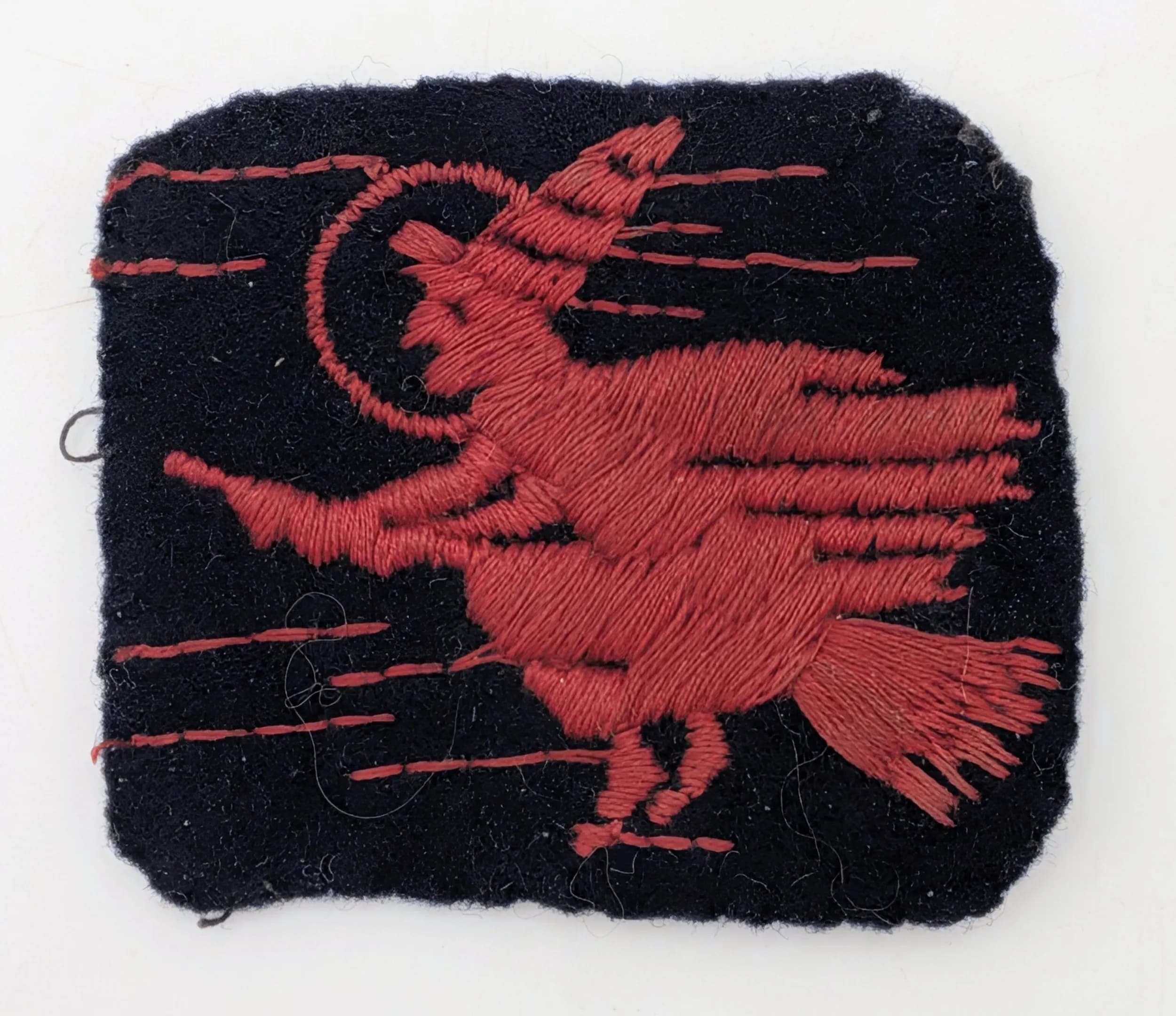 A WW2 Era, Red Witch Cloth Badge of the 2nd Anti-Aircraft Division of the Royal Artillery. 1935-42. 'We Sweep the Skies'. 5 x 4.5cm.