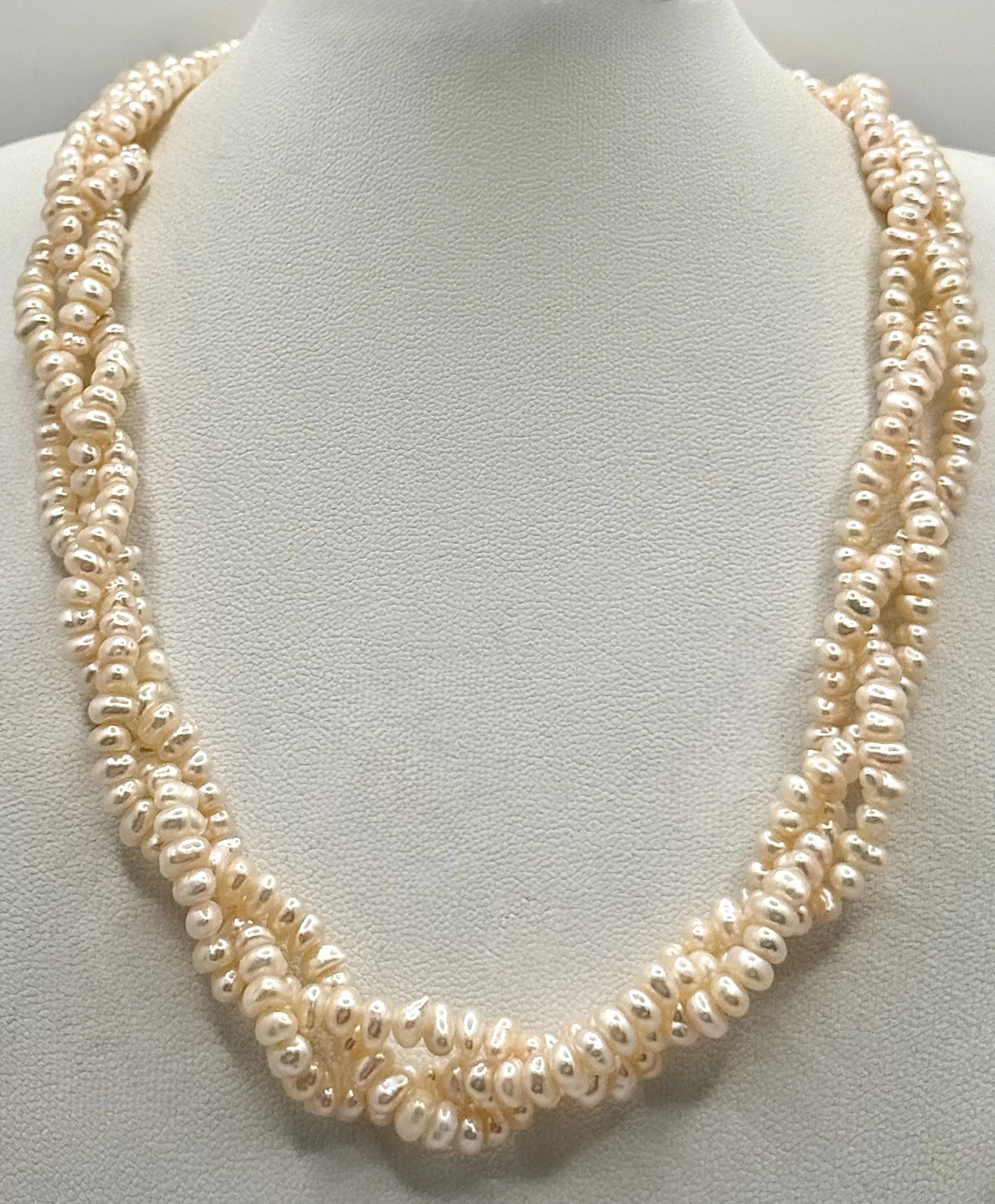 A beautiful Three-Strand Braided Freshwater Pearl Necklace. Comprising three strands of irregular pink tone freshwater pearls in a braided design, with a cylindrical magnetic clasp. Approx. 39.8cm length.