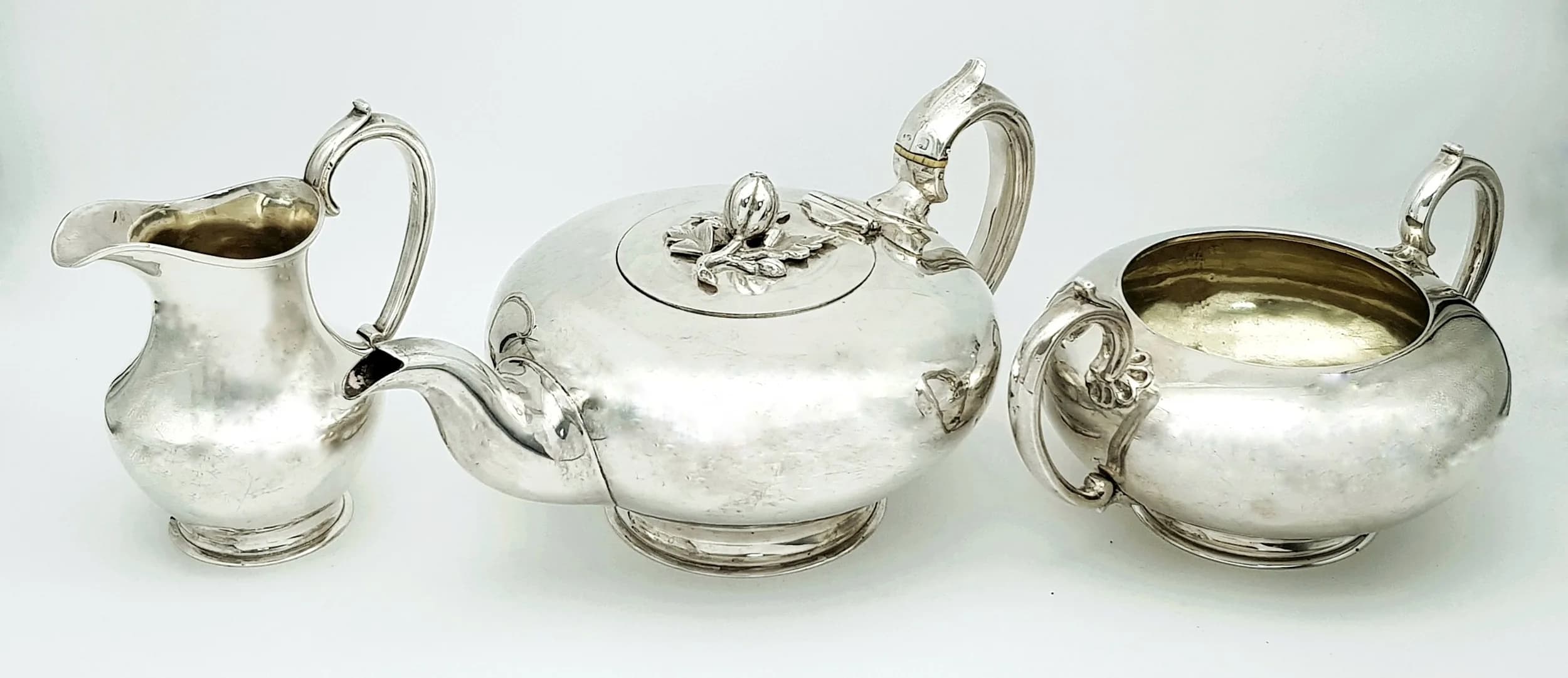 A BEAUTIFUL ENGLISH STERLING SILVER TEA SET MADE IN LONDON IN 1843 WEIGHING 1.2kgs THE LOW ROUNDED SHAPE IS CLASSIC 19th CENTURY AND FEATURES A CRAFTED FRUIT AND LEAF FINIAL AND COMING WITH A SUGAR BOWL AND CREAMER ALL IN GENERALLY GOOD CONDITION(THE TEAPOT HAS A COUPLE OF VERY SMALL DENTS FROM USE)